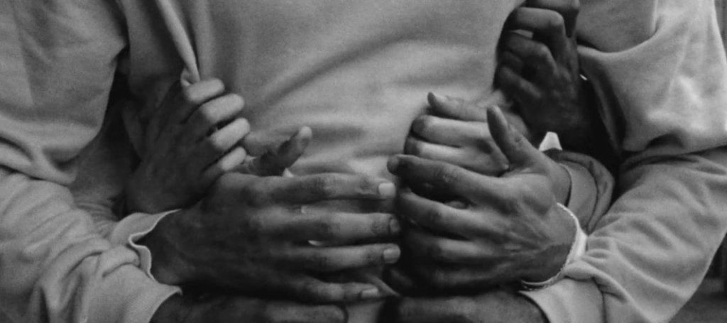 B&W closeup of 7 hands reaching around to hug someone.