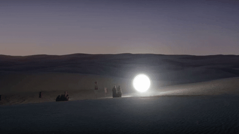 "Two people stands next to an orb of light floating over the desert at sunset" from A Thousand Suns
